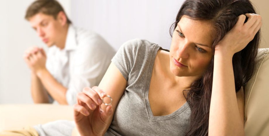 Женщина сидит на диване с обручальным кольцом в руке, рядом мужчина в задумчивости