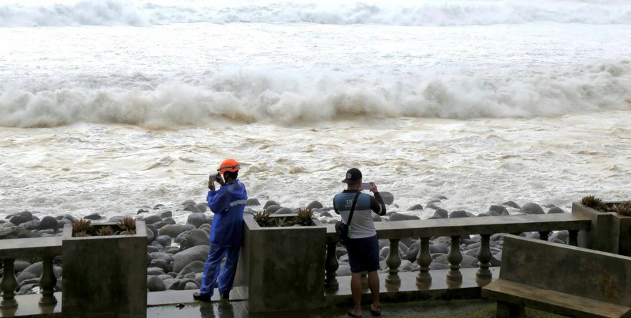 Двое жителей фотографируют огромные волны на побережье Филиппин, где ощущается приближение супертайфуна "Рагаса"