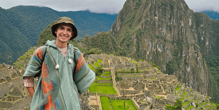 Мужчина в пончо стоит на фоне древних террас Мачу-Пикчу в Перу