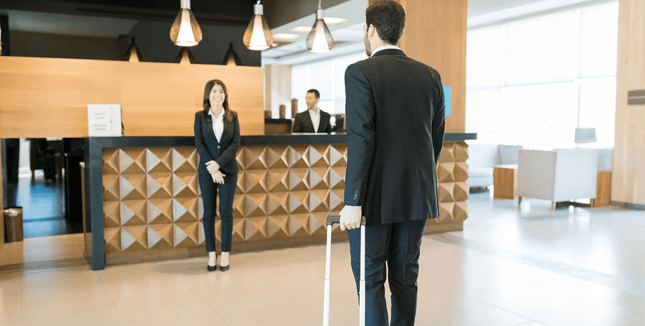 Сотрудница отеля улыбается и приветствует постояльца в современном холле