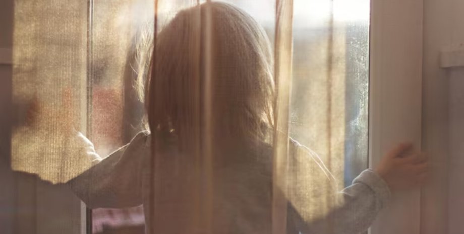 Ребёнок стоит у окна с занавеской, девочка увидела "собаку", из-за которой боялась идти в туалет