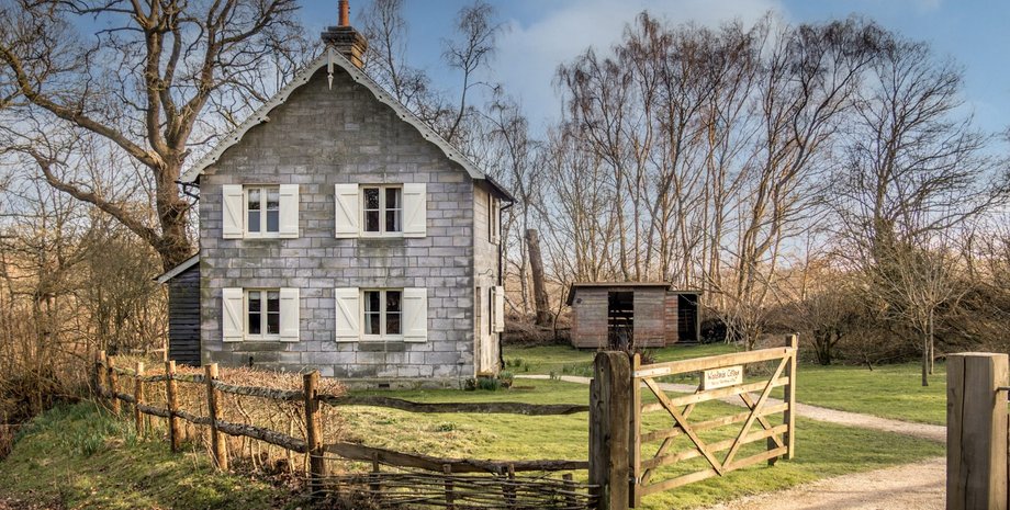 Старинный дом с закрытыми ставнями, окруженный забором и деревьями