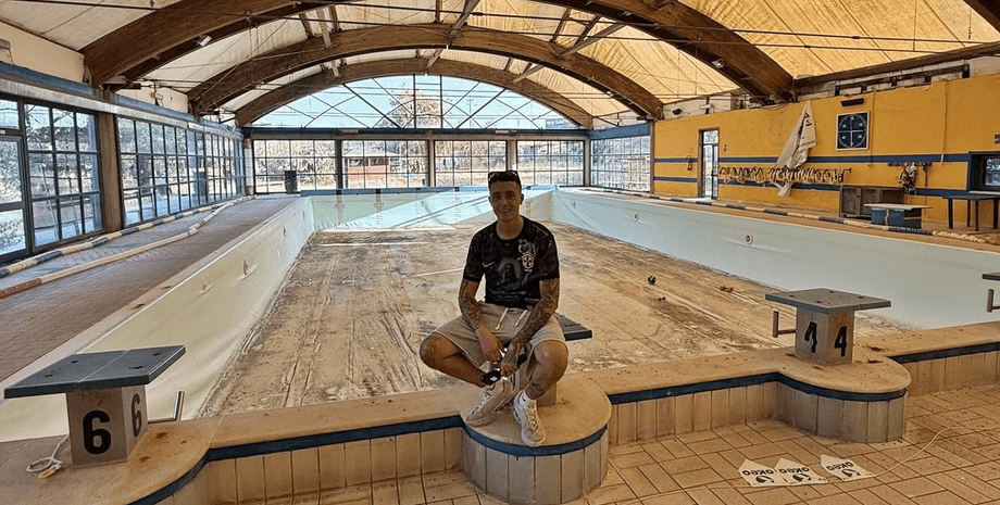 Мужчина сидит у пустого крытого бассейна в заброшенном отеле