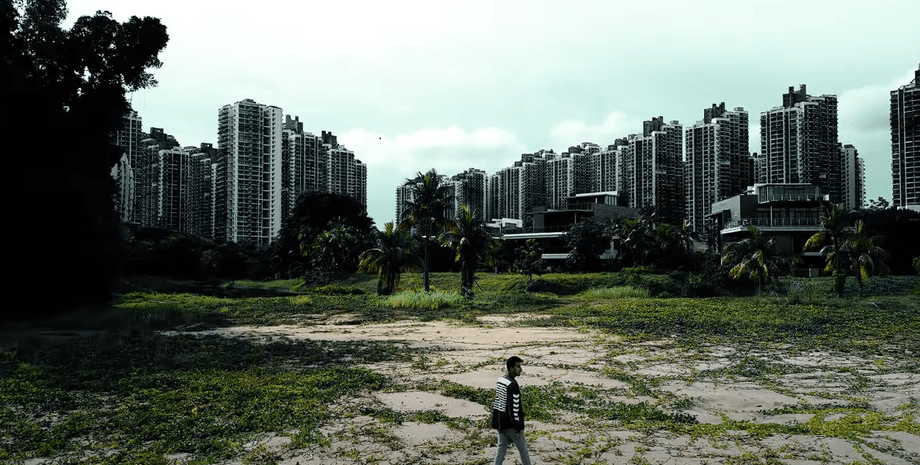 Мужчина идет по заброшенной территории на фоне огромных, но пустых жилых комплексов Forest City