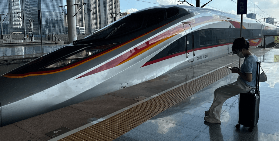 Пассажирка сидит на чемодане на перроне рядом с высокоскоростным китайским поездом на современном вокзале