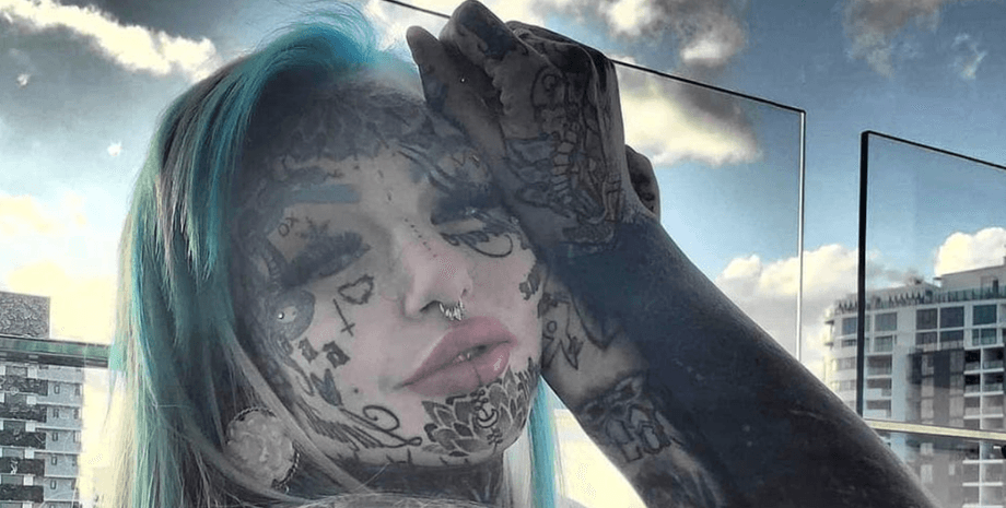 Модель Эмбер Люк с полностью покрытым татуировками лицом и руками, позирующая на улице на фоне города