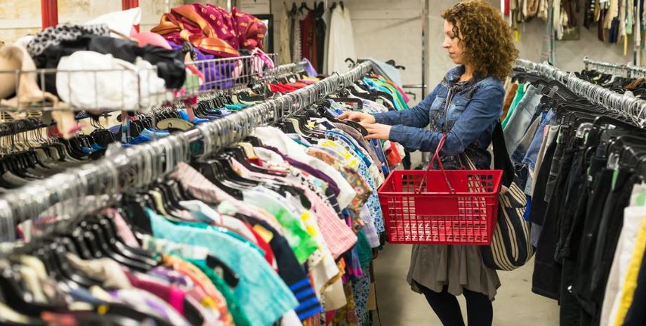 Женщина рассматривает одежду на вешалках в магазине секонд-хенда в поисках интересных вещей