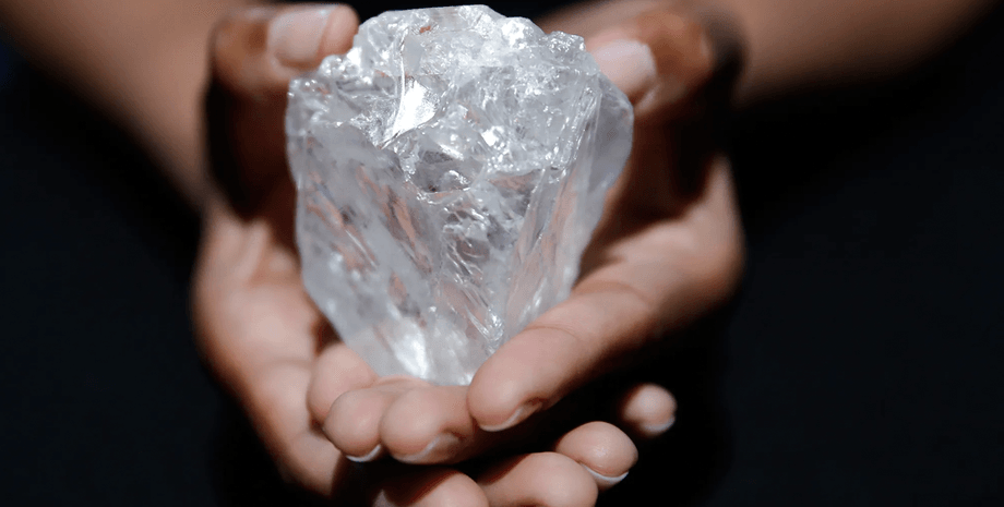 Необработанный прозрачный алмаз крупного размера в руках человека