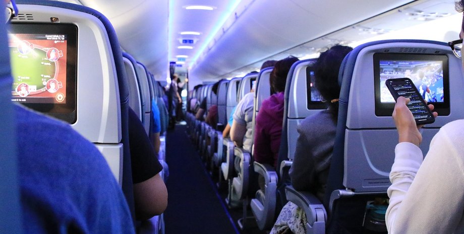 Пассажиры в салоне самолета смотрят фильмы на экранах перед собой