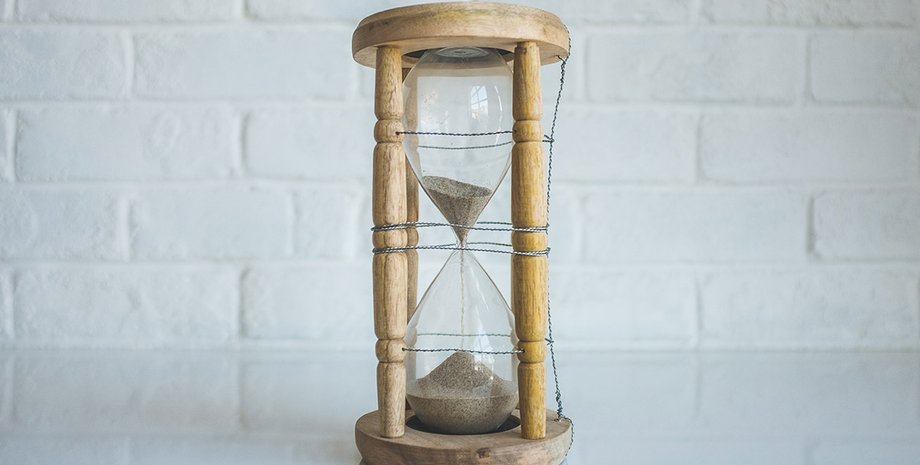 Песочные часы на фоне белой стены символизируют течение времени и идею его возможного искажения
