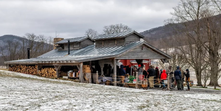 Группа людей у деревянного сахарного домика с металлической крышей, где варят сок для кленового сиропа