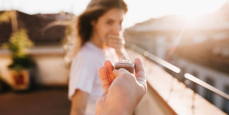 Мужчина протягивает коробочку с кольцом женщине во время романтического предложения