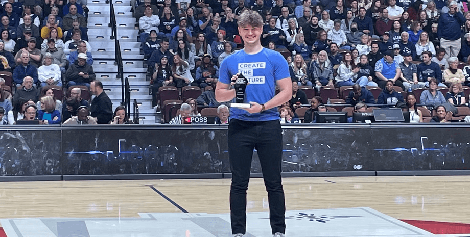 Молодой миллиардер и сооснователь Mercor Брендан Фуди стоит на арене с наградой в руках перед большой аудиторией