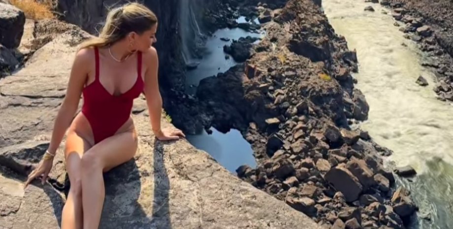 Женщина в красном купальнике сидит на краю скалы у водопада Виктория, не подозревая, что за ее спиной ползает змея