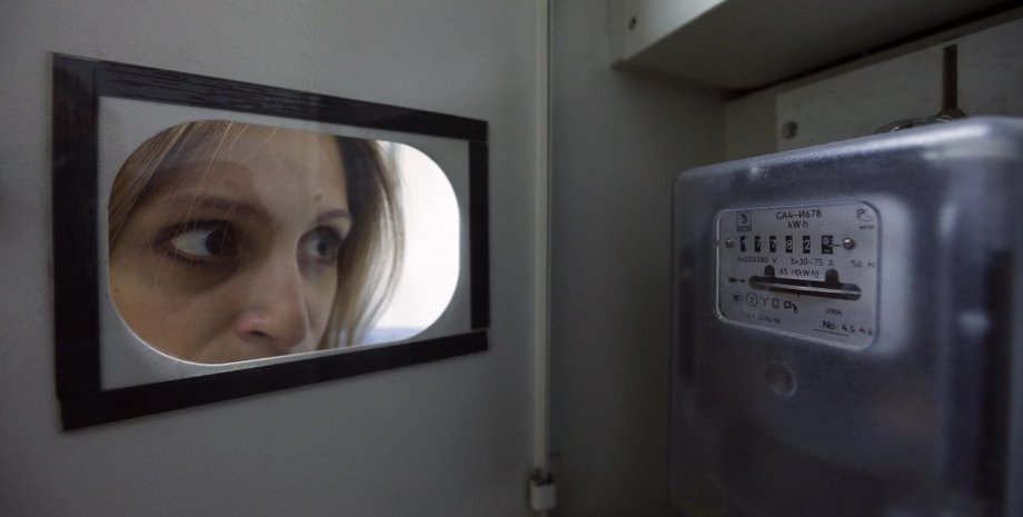 Женщина внимательно смотрит на электросчетчик, проверяя показания и потребление энергии